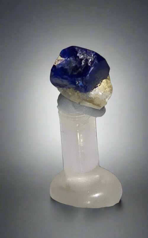 Vivid blue sapphire crystal on matrix, displayed on clear quartz stand