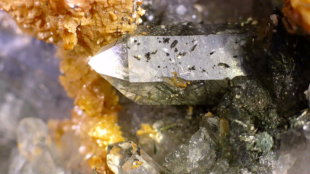 Clear quartz crystal with black inclusions, embedded in orange matrix, mineral specimen